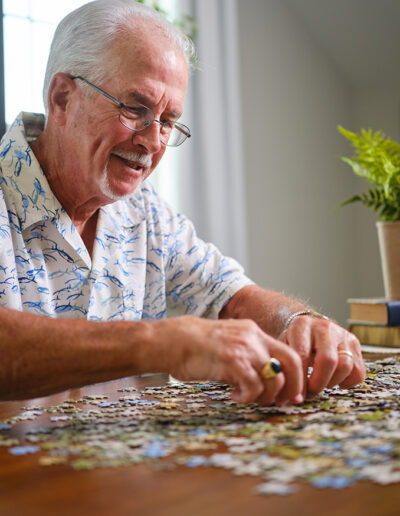 Man does a puzzle in a plue and white shirt at the Presbyterian Life Plan Community