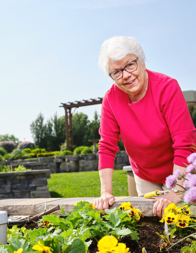 Woman with a bright pink shirt overlooks her garden at the Quarryville Retirement community with pride.